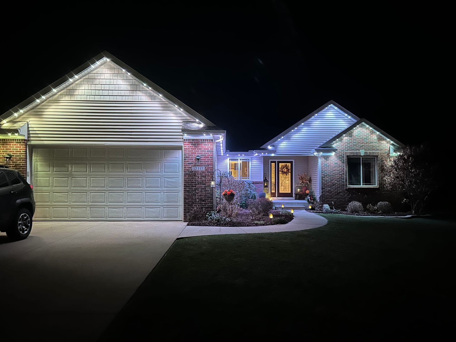 Cool white permanent roofline lights on a brick home with a large garage gable and front entry gable