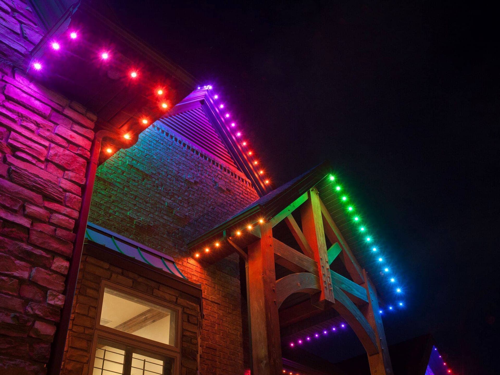 Close-up of multicolour permanent roofline lights running along the gables of a stone home with a timber-frame porch