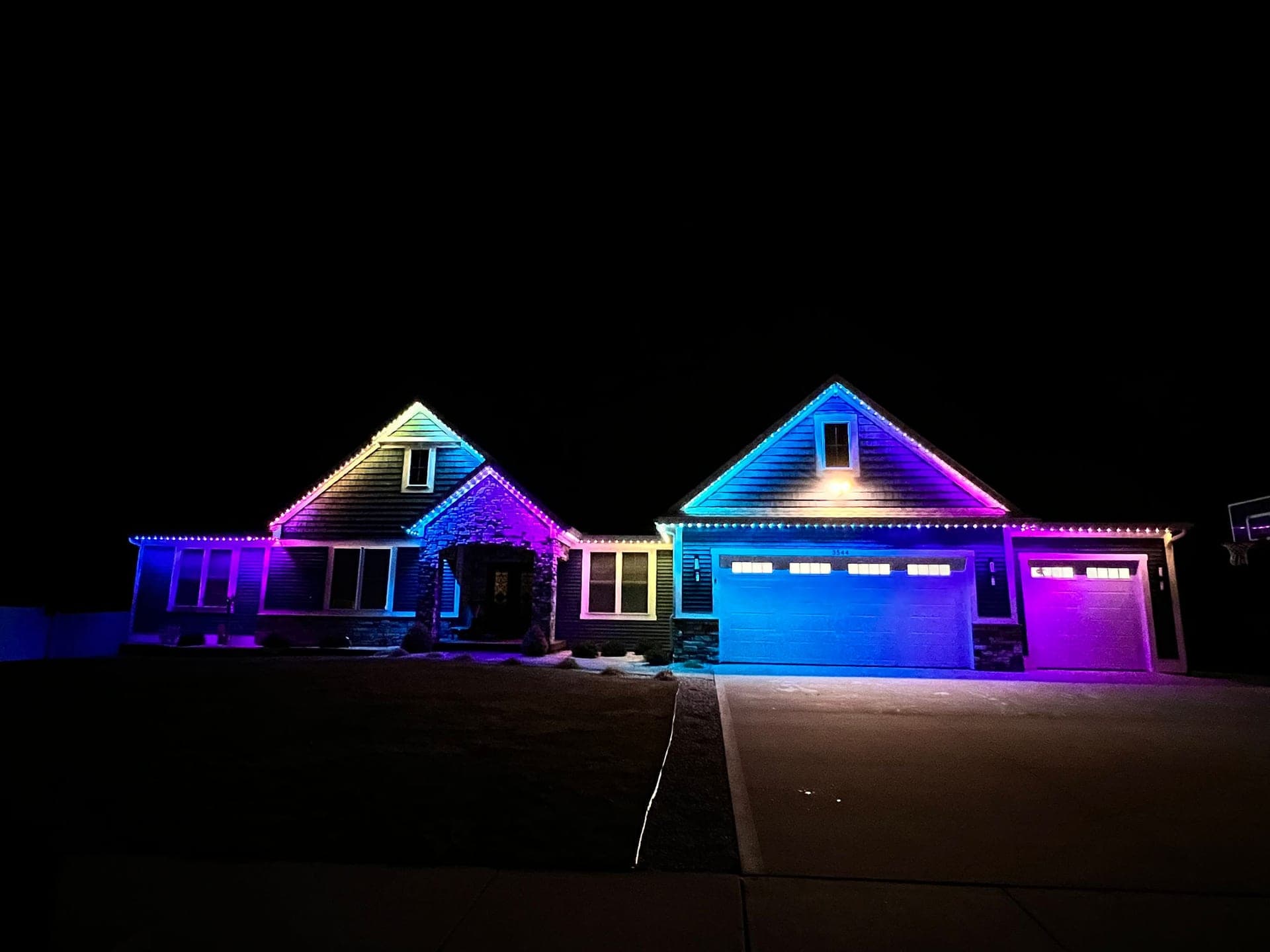 Purple and blue permanent roofline lights on a dark-sided bungalow with a double garage and stone entry