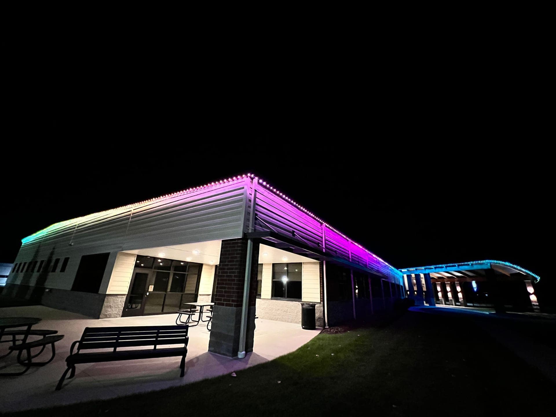 Purple and teal permanent roofline lights on a single-storey commercial building with a lit walkway canopy