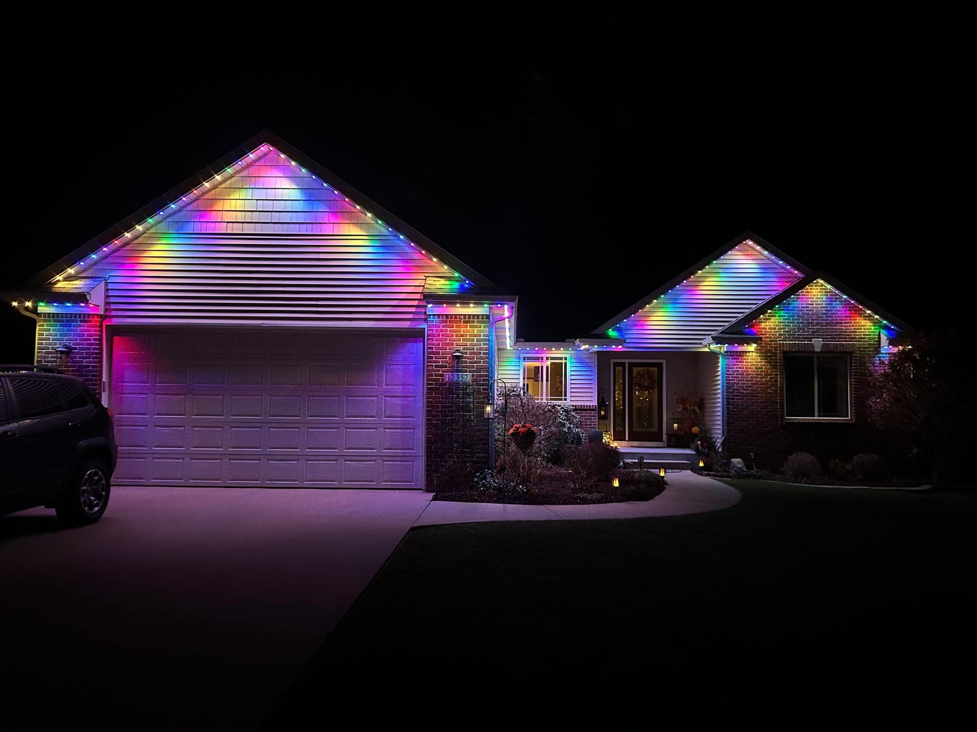 Rainbow permanent roofline lights on a brick home with a large garage gable, the same system shown in holiday mode