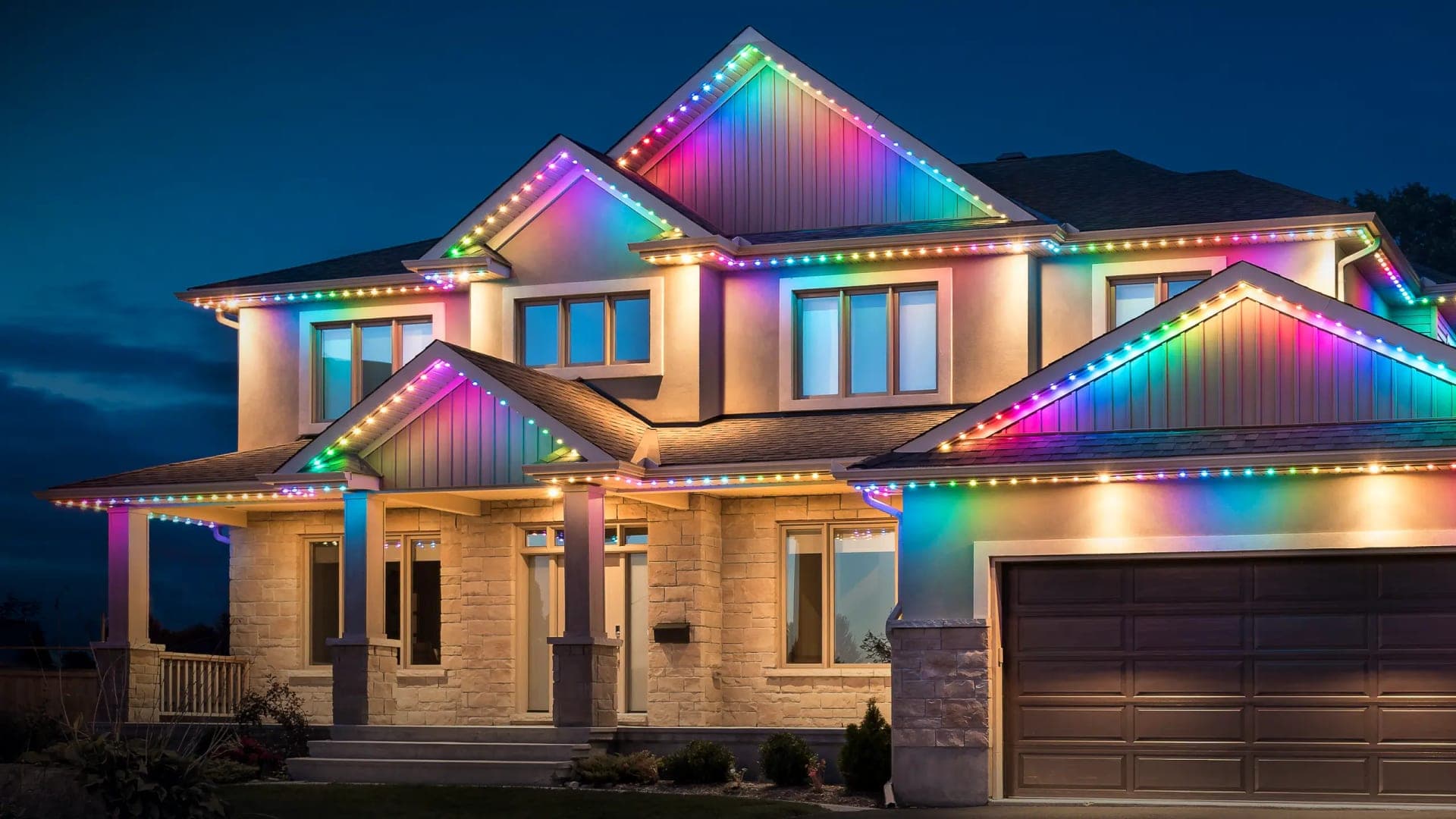 Two-storey stone and siding home with permanent roofline LED lights in a rainbow gradient along every peak, eave and gable