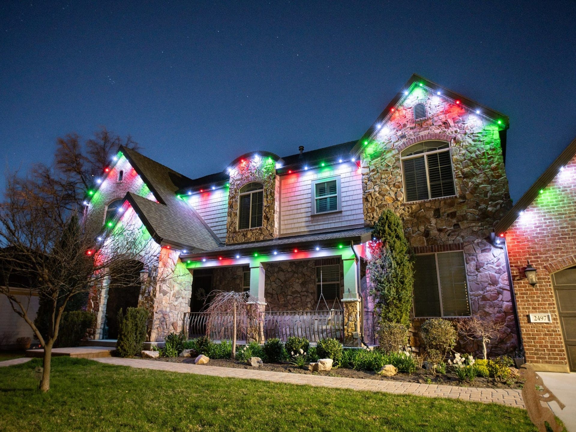 Red, green and white permanent roofline lights outlining the steep gables of a stone and siding two-storey home