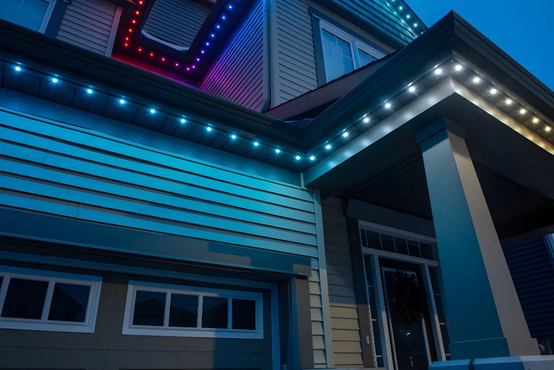 Close-up of teal permanent LED soffit lights in a colour-matched track along the eaves of a grey-sided home