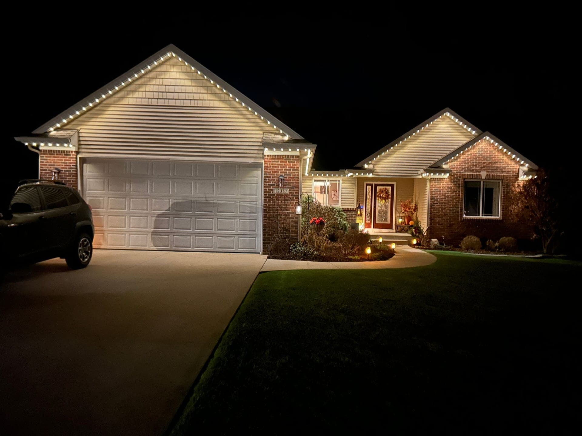Warm white permanent roofline lights on a brick home with a large garage gable, shown in everyday architectural mode