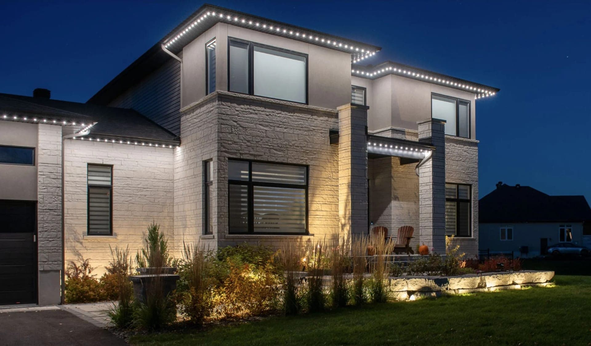 Crisp white permanent roofline lights tracing the flat roof lines of a modern stone and stucco home