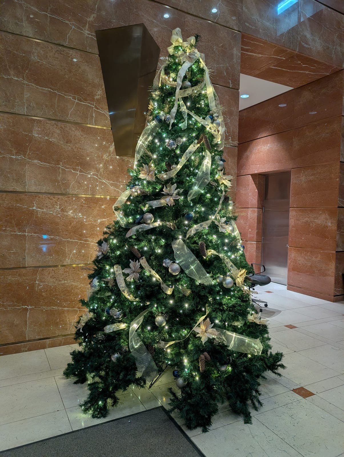 Close-up of a corporate atrium Christmas tree with gold ribbon, poinsettias and silver ornaments