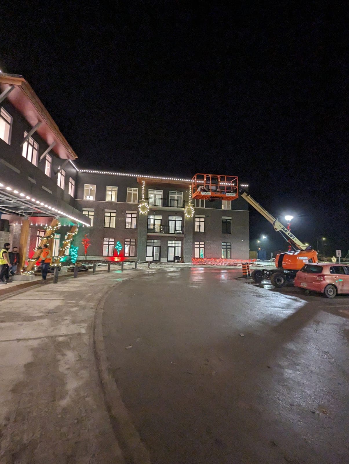 Crew installing warm white roofline Christmas lights on a commercial building with a boom lift at night.