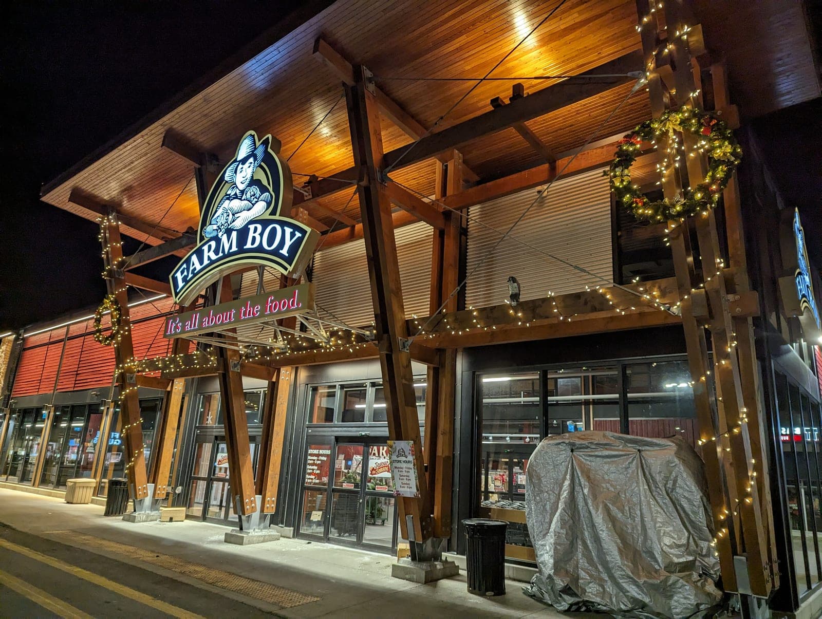 Wide view of a commercial building facade decorated with warm-white Christmas string lights and a wreath