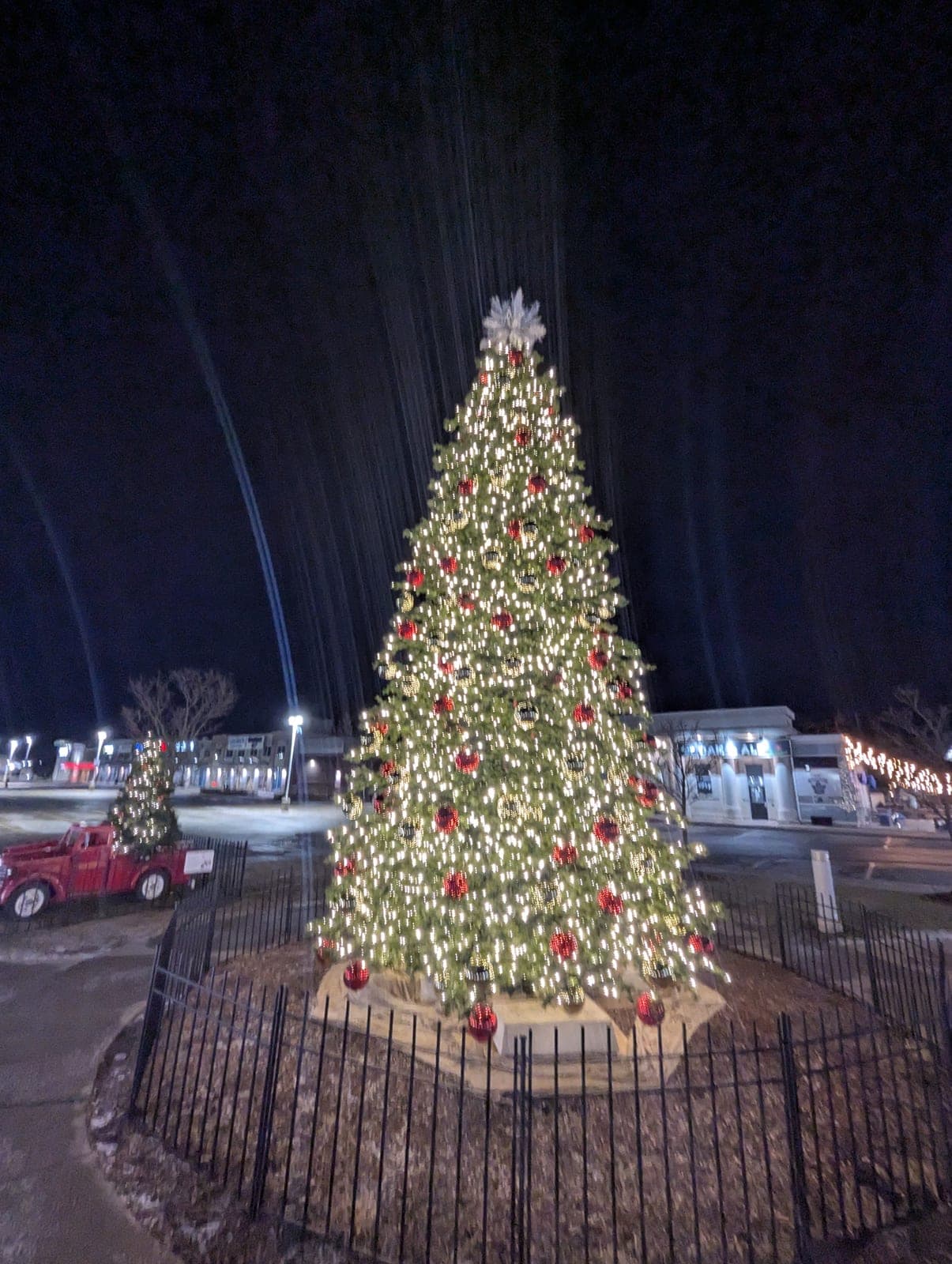 Commercial Christmas tree lit at night beside a vintage fire truck in a shopping plaza