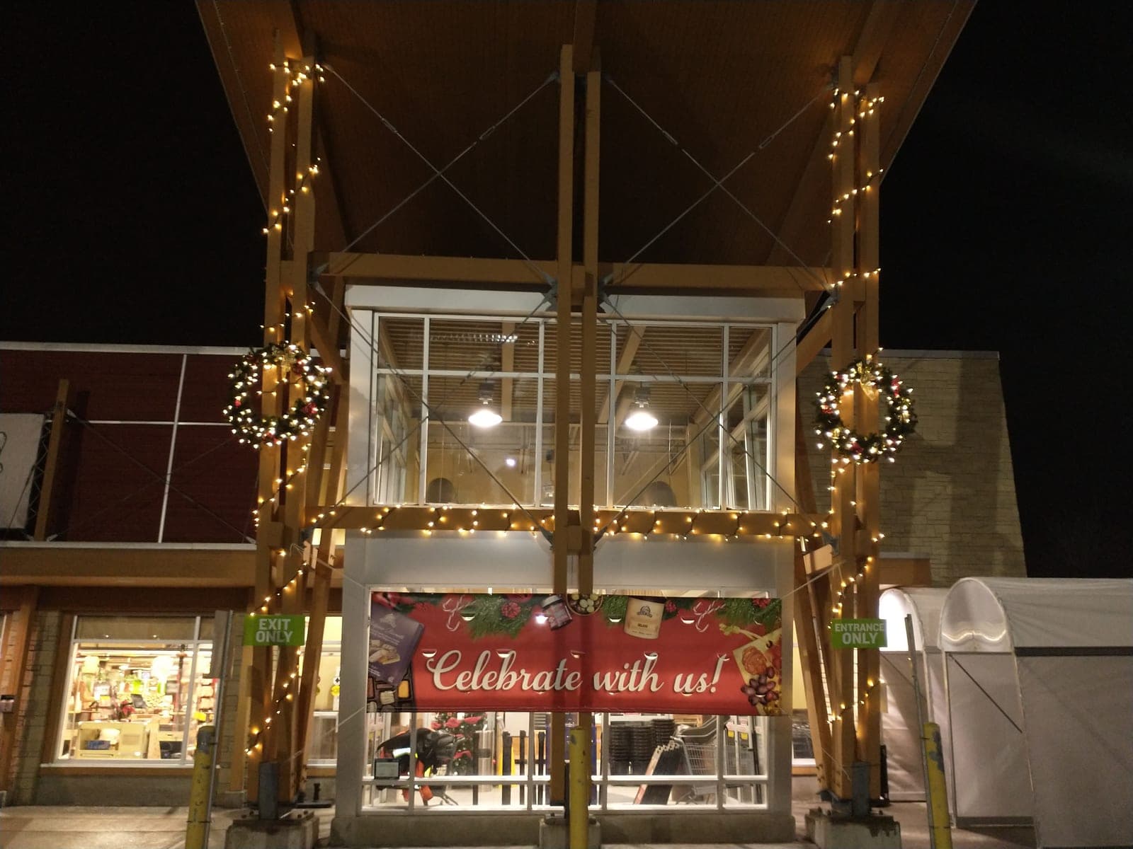 Commercial entrance canopy with warm-white string lights and lit Christmas wreaths on wooden posts
