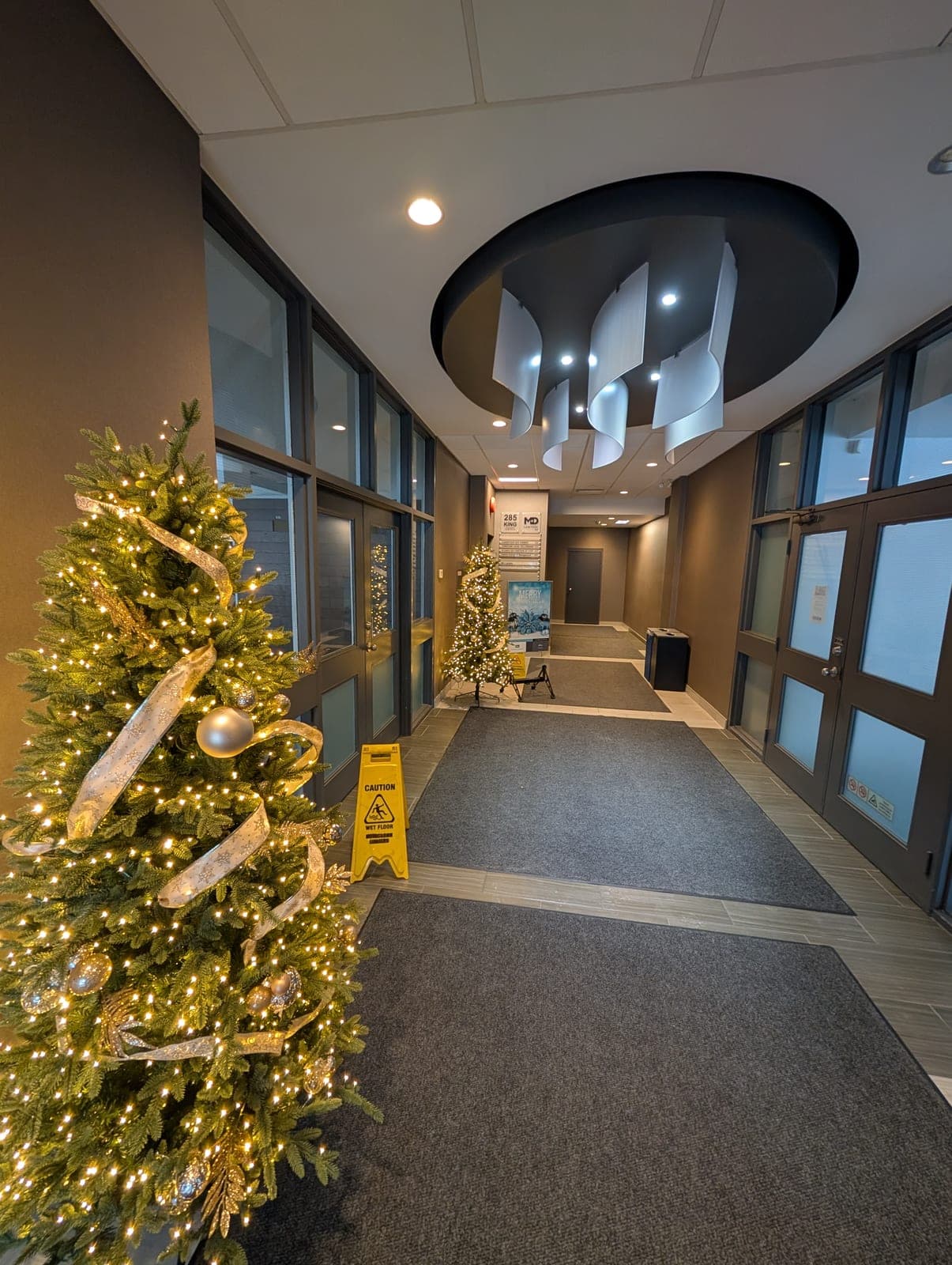 Decorated Christmas tree with gold ribbon and warm-white lights in a modern commercial office lobby
