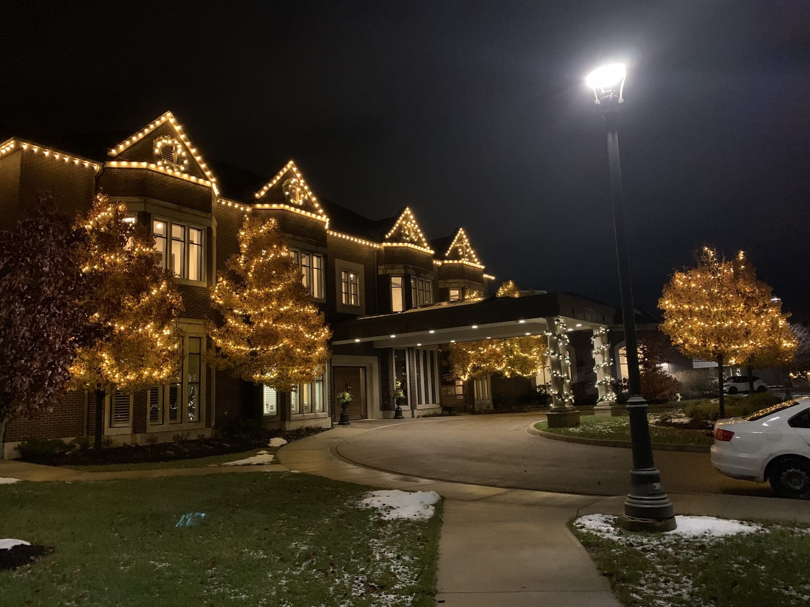 Estate venue with warm-white roofline Christmas lights and a covered entrance wrapped in lights at night
