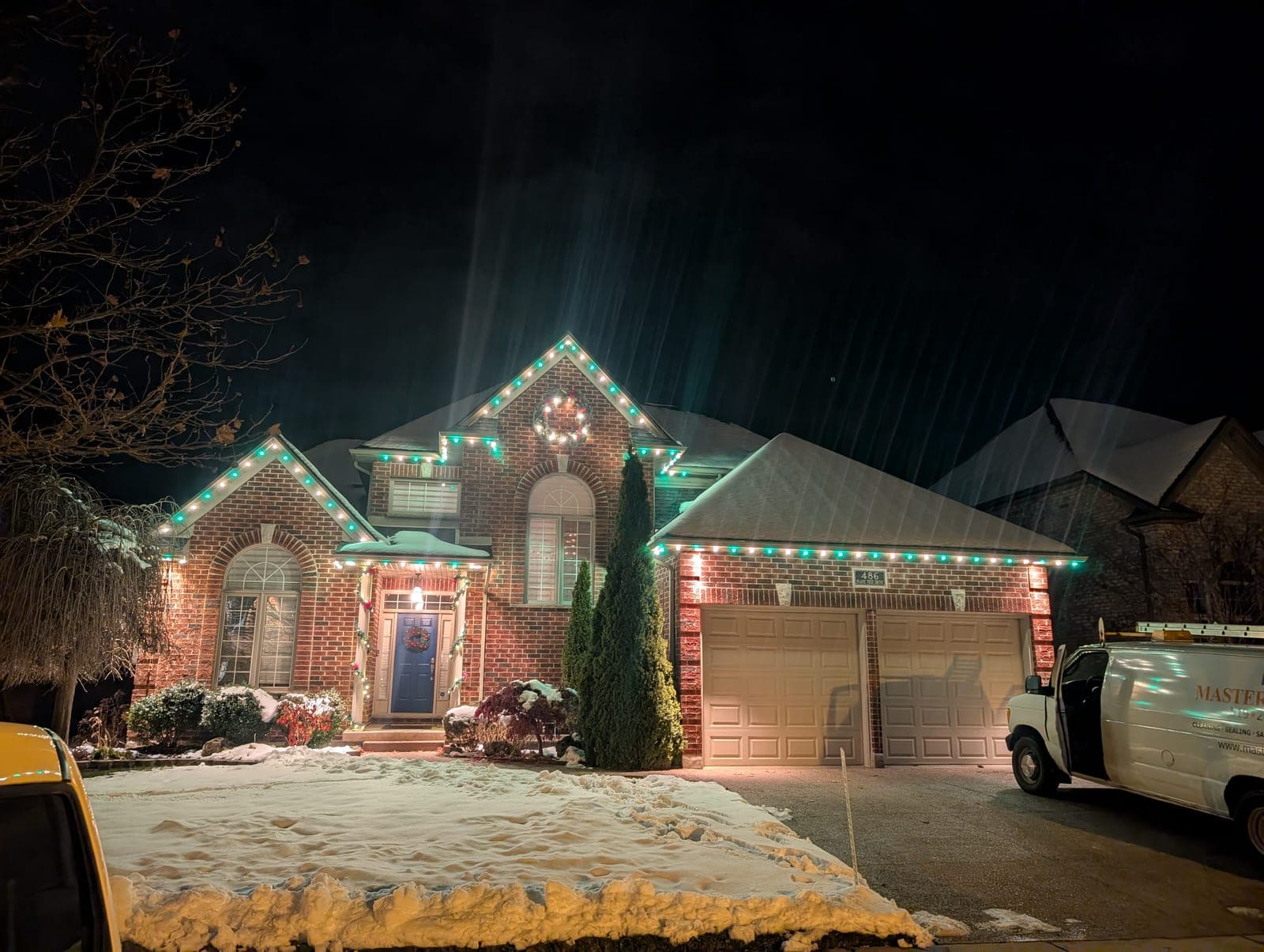 Brick home outlined in green and warm roofline Christmas lights on a snowy evening