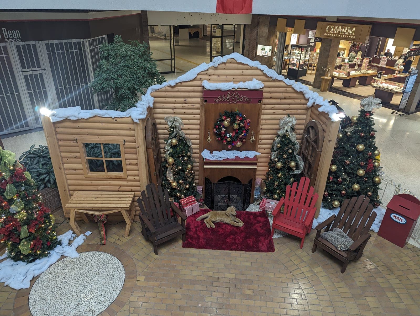 Overhead view of a mall Santa's log cabin photo set with snow-topped roof, wreath, Adirondack chairs and decorated Christmas trees