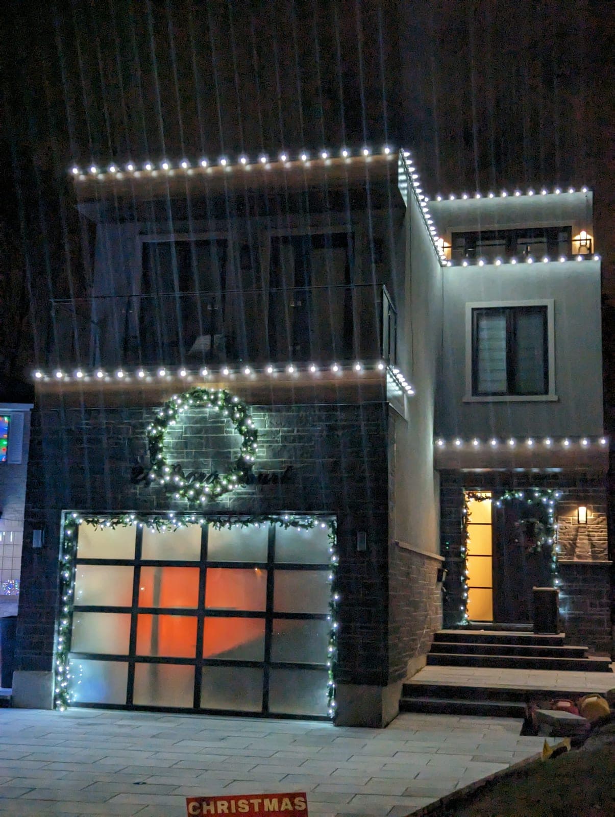 Modern two-storey home with warm-white roofline Christmas lights and a lit wreath above the garage
